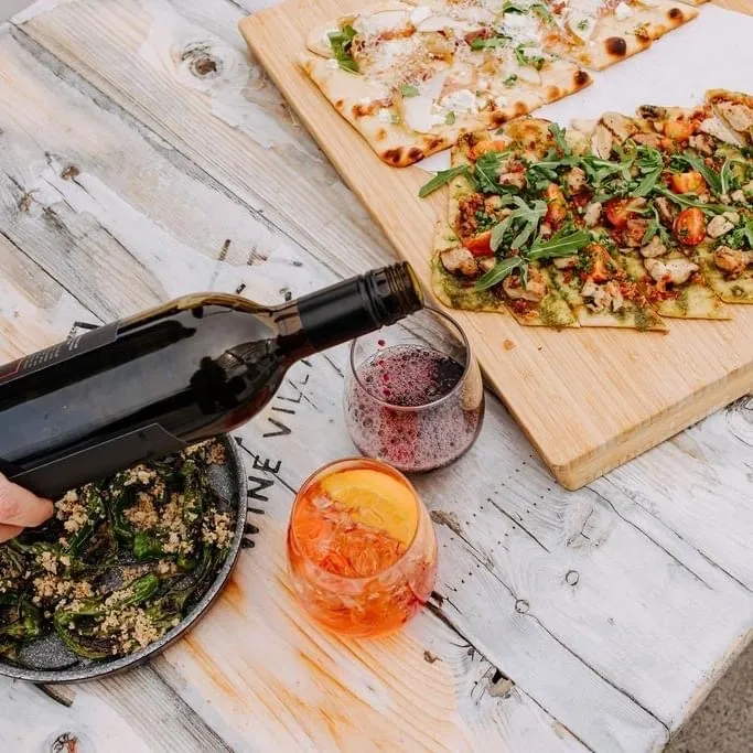 Pizza and salad on a district wine village patio seat with a bottle of wine pouring into a glass over a cocktail